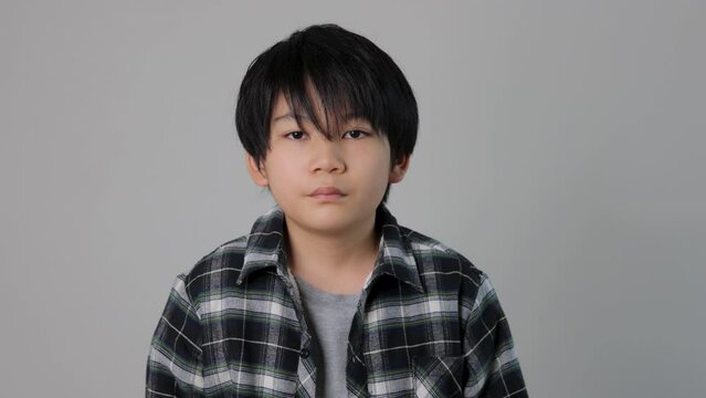 Young asian teenager looks at the camera uncomfortably. White background.