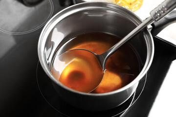 Saucepan and ladle with used cooking oil on stove, closeup