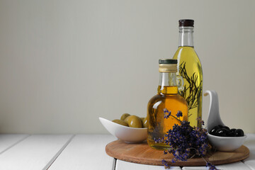 Different cooking oils and ingredients on white wooden table against light background, space for...