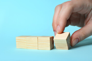 Woman arranging cubes on light blue background, closeup. Idea concept