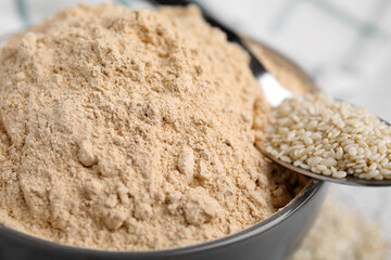 Sesame flour in ceramic bowl and spoon of seeds, closeup