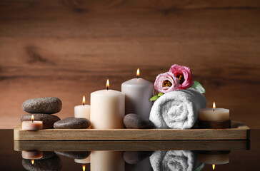Beautiful composition with spa stones, flowers and burning candles on mirror table against wooden background