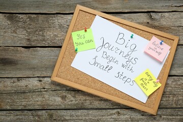 Corkboard with motivational quotes on wooden table, top view