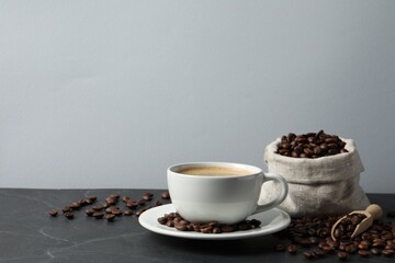 Cup of aromatic coffee and beans on grey table. Space for text