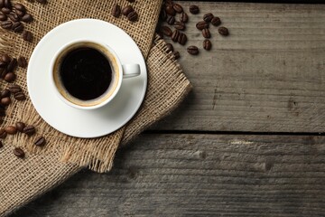 Cup of hot aromatic coffee and roasted beans on wooden table, flat lay. Space for text