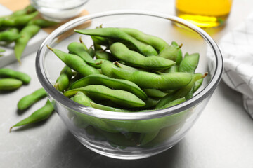 Bowl with green edamame beans in pods on light grey table, closeup