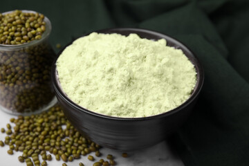 Mung bean flour in bowl and seeds on white marble table, closeup