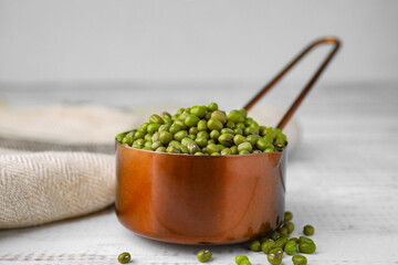 Scoop with mung beans on white wooden table, closeup