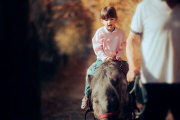Little Girl Riding a Pony Held by an Instructor. Toddler kid joined by the equestrian monitor in her horseback ride
 - obrazy, fototapety, plakaty