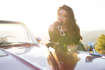 beautiful girl in retro style posing near vintage red cabriolet car.