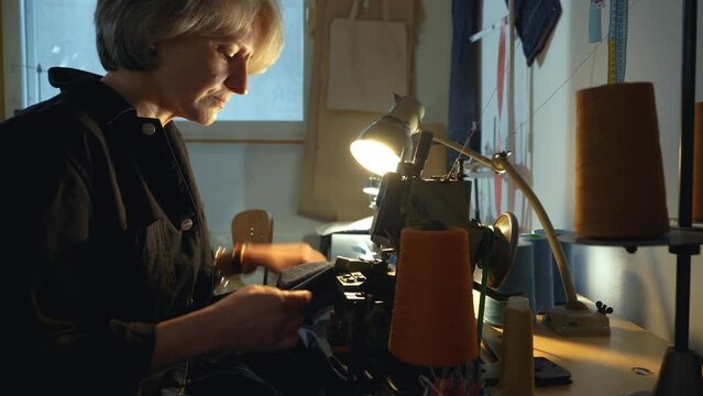 A female tailor seamstress hemming old jeans with vintage authentic machine in in a workshop repairing old denim clothes. Small family business, tailoring and repair of clothes, handmade, startup.