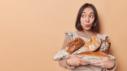 Wondered young Asian woman carries freshly baked loaves of bread looks amazed aside smeared with...