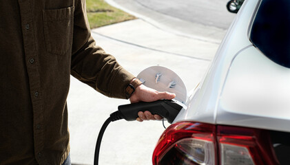 Man is charging electric car or EV car or electric vehicle on his driveway at home. Home station charging for zero emission and future energy.