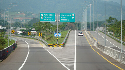 Trans Java toll road at noon. There are signs for the city of Surabaya, Malang, Purwodadi, Pandaan,...