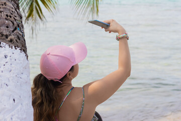 Latin woman with pink hat on the beach taking a selfie