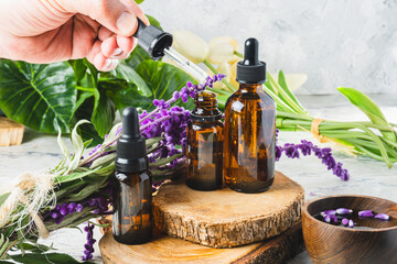 Hand taking essential oil from a bottle with a dropper in the middle of leaves and flowers