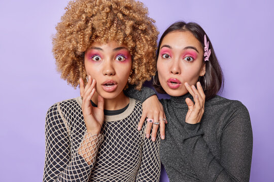 Shocked stupefied women stare at camera have vivid makeup apply pink eyeshadow cannot believe in something amazing stand closely to each other against purple background. Feminine and beauty.