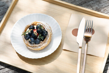Blueberry tart with knife and fork on wooden tray in natural light.