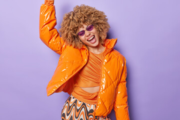 Fashionable stylish woman wears trendy sunglasses and orange jacket dances carefree feels like...