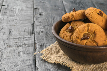 A clay bowl with homemade cookies on a wooden table.