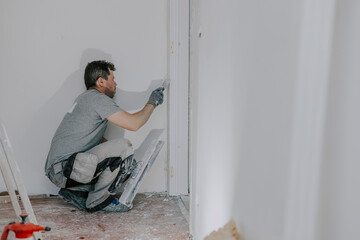 A young builder is plastering a doorway.