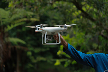 white drone flying between trees in forest