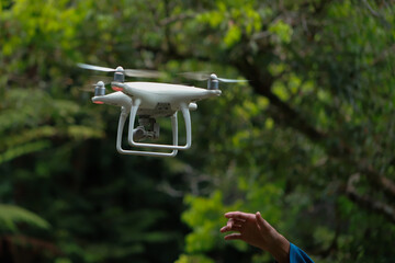 white drone flying between trees in forest