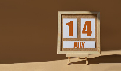 July 14th. Day 14 of month, Calendar date. Cork board, easel in sunlight on desktop. Close-up, brown background.  Summer month, day of year concept