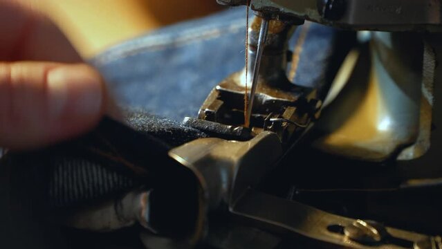 A female tailor seamstress hemming old jeans with vintage authentic machine in in a workshop repairing old denim clothes. Small family business, tailoring and repair of clothes, handmade, startup