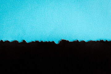 Torn half sheet black paper horizontal on blue paper at the bottom. As template for message or advertisement.