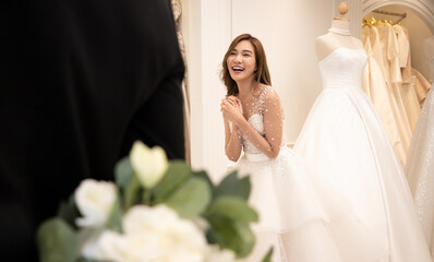 Asian woman in a bridal gown bright smiling. The groom wearing black suit holds a white bouquet of...