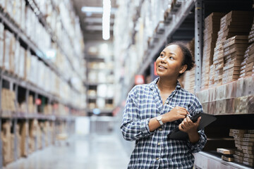 Portrait of young attractive African American woman auditor or trainee staff work looking up stocktaking inventory in warehouse store by computer tablet and stylus near products shelf.
