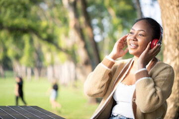 Portrait of young brunette woman wearing coat listening to music with headphones and smiling while leisure in autumn park