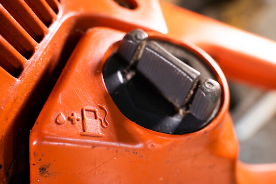 Tank for filling the fuel mixture with oil in the chainsaw. Gas station and lubricant symbol on the body of an orange chainsaw. Oil for lubricating a two-stroke engine. Fuel filler neck close-up