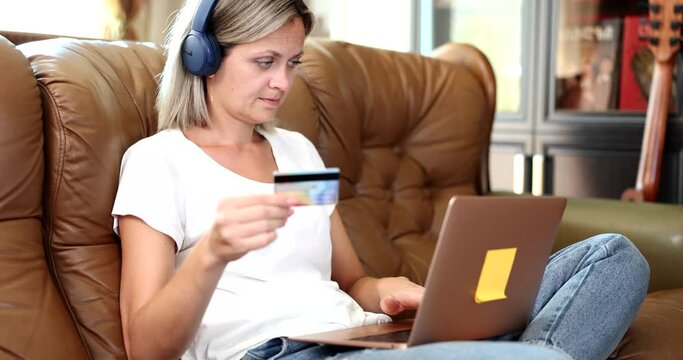 Woman in headphones and with bank card pays for language courses online on a laptop
