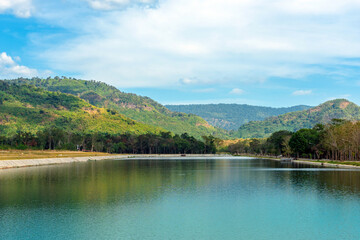 Fototapeta na wymiar Beautiful and peaceful view of large reservoir with surrounding mountain and trees in beautiful sunshine and cloudy sky in Thailand. Tranquil and beautiful natural scenery landscape of reservoir lake.
