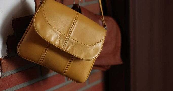 Yellow and brown leather bag hangs on hanger against wall