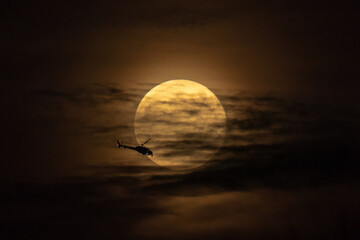 Helicopter is flying trough the full moon during at night. Helicopter halo on background full moon
