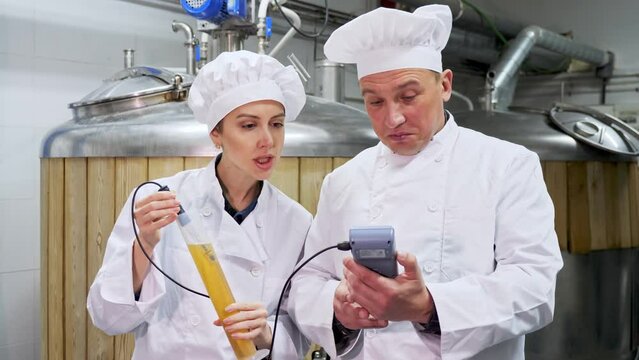 Man and woman brewmasters measuring strengh of beer sample with alcoholometer.