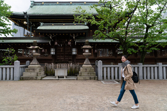 full length of Asian Japanese female tourist walking past a temple building with green rooves while exploring Osaka Tenmangu Shrine in japan at springtime