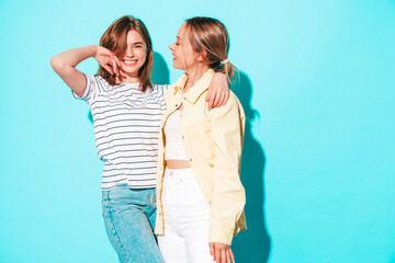 Two young beautiful smiling brunette hipster female in trendy summer clothes. Sexy carefree women posing near blue wall. Positive models having fun. Cheerful and happy