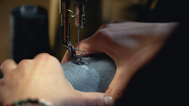 A female tailor seamstress repair old jeans with vintage darning machine in a workshop repairing denim clothes. Small family business, tailoring and repair of clothes, handmade, startup. Close-up