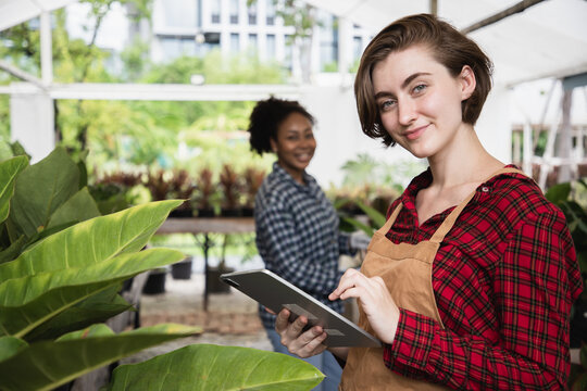 Happy charming woman gardening wearing denim apron with digital tablet for checking order in home gardening for looking who buys the tree and ornamental.
