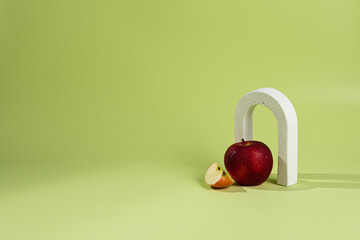 An empty stage with one white concrete arch under it a red apple. On a green background and a shadow from sunlight