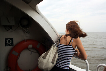 A young girl with long brown hair floats on the ship. A woman stands with her back in the frame. A man at the side of the ship looks at the water