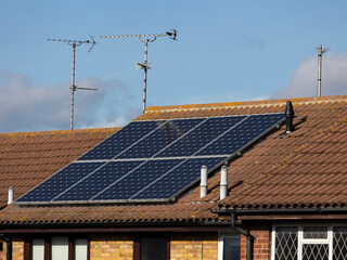 Roof on a house with solar panels and analogue TV aerials against blue sky