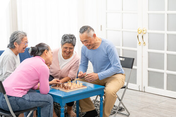 Asian senior people men and women in casual playing chess at nursing home, sitting around table. Asian Senior Elderly male spend leisure time. Happy smiling Older mature man enjoy activity in house.