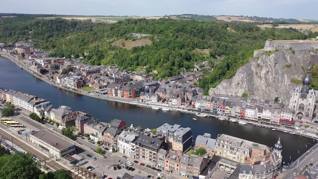 Scenic summer view of Dinant cityscape on banks of river Meuse overlooking Collegiate Church of Notre Dame and fortified Citadel on top of cliff overgrown with green trees, Namur province, Belgium