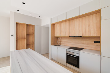 Modern kitchen interior with island and wooden furniture. Empty and bright refurbished apartment.