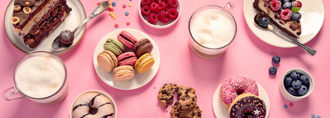 Table with various cookies, donuts, cakes, coffee cups on pink background.